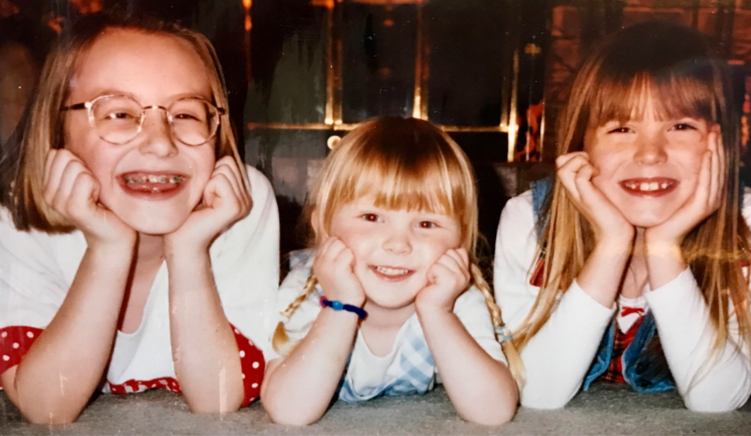 young Kami Zahner laying on the floor smiling with two other girls