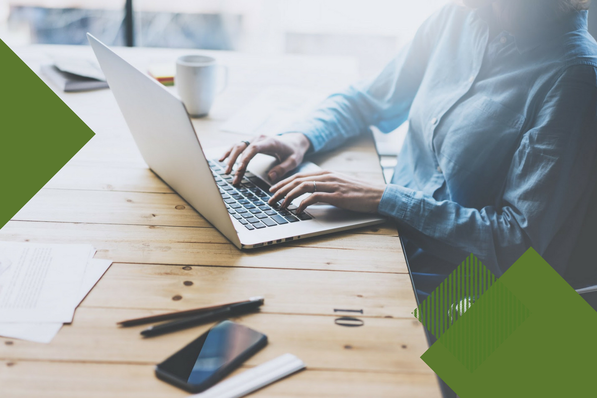 person sitting at a wooden table typing on a computer, image has dark green square shapes around edges