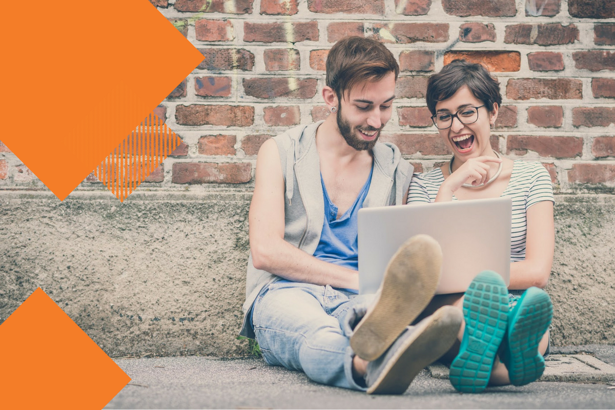 Young man and woman sitting on the ground laughing with a computer on lap