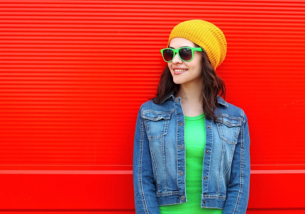 woman in yellow hat stands against bright red wall